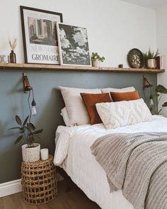 a bed with pillows and blankets on top of it next to a wooden shelf filled with potted plants