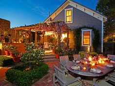 an outdoor dining table with candles on it in front of a house at night time