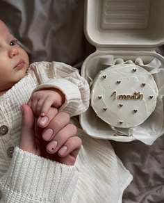 a woman holding a baby in her arms next to a cake with the word i month written on it