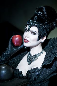 a woman with black makeup and an apple in her hand is posing for the camera