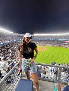 a woman standing on the bleachers at a baseball game holding a drink in her hand