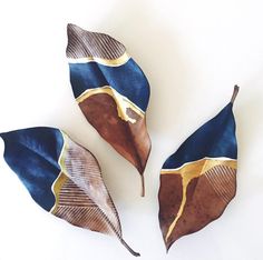 three blue and gold leaves on a white surface with one brown leaf in the middle