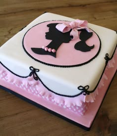 a pink and white cake with black silhouettes on the top is sitting on a wooden table