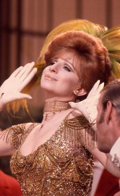 a woman with red hair wearing a gold dress and white gloves, standing in front of other people