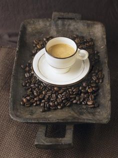 a cup of coffee sitting on top of a pile of coffee beans in a square tray