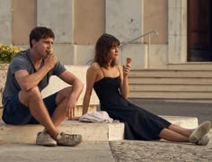 a man and woman sitting on the ground eating ice cream