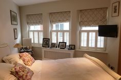 a white bed sitting in a bedroom next to two windows with shutters on them