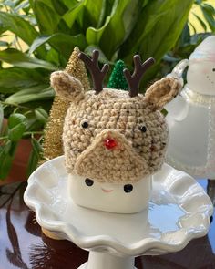 a crocheted reindeer hat sitting on top of a white plate next to potted plants