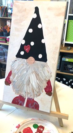 an easel with a painting of a gnome on it next to a paper plate