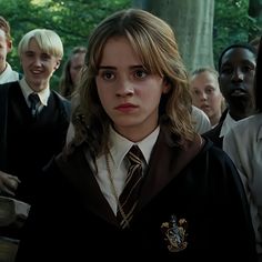 a group of people standing around each other in front of trees and bushes, with one person wearing a harry potter costume