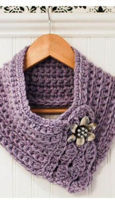 a purple crocheted scarf hanging on a wooden hanger next to a white wall