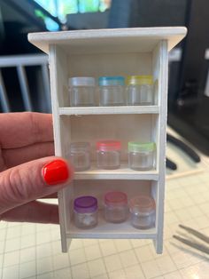 a hand is holding a miniature shelf with many small jars and containers on it's sides