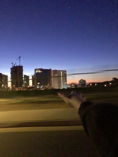 a person is holding their hand out the window at night with city lights in the background