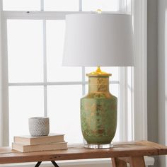 a green vase sitting on top of a wooden table next to a white shade lamp