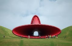 people standing in front of a large red object on top of a green hill with grass