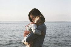 a woman holding a baby near the water