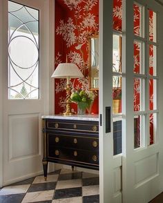 an entry way with red and white wallpaper, checkered flooring and a black chest of drawers