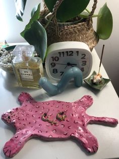 a clock sitting on top of a white table next to a pink animal shaped object