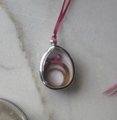 a close up of a coin and a pendant on a marble counter top with pink ribbon