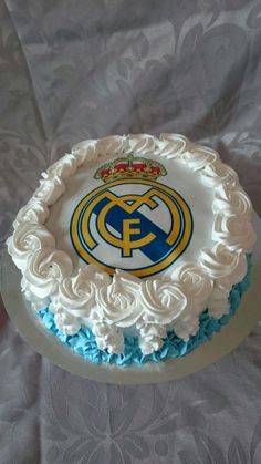 a white cake with blue frosting and a real madrid crest on it