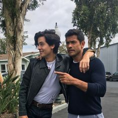 two young men standing next to each other in front of a tree and fenced area