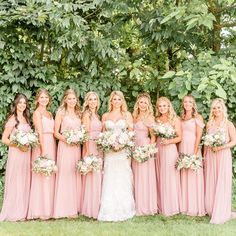 a group of women standing next to each other in front of some bushes and trees