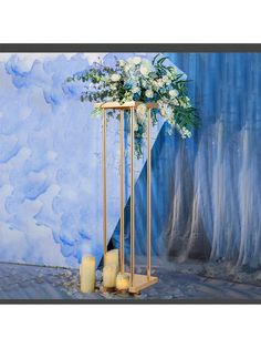 a tall metal stand with flowers and candles on it in front of a blue backdrop