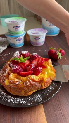 a pastry with strawberries on it sitting on top of a table next to yogurt cups