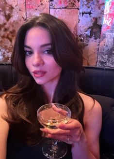 a woman sitting at a table holding a wine glass in her hand and looking into the camera