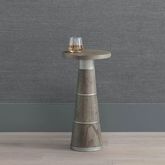 a small wooden table with two glasses on it and a grey wall in the background