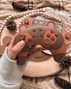 a person holding a game controller in front of a wooden plate with pine cones on it