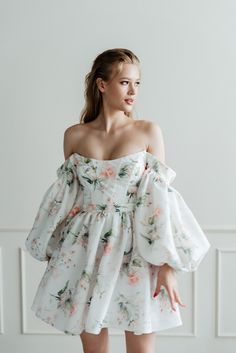 a woman wearing a white dress with flowers on it, posing in front of a wall