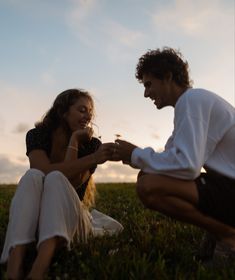 a man kneeling down next to a woman on top of a lush green field at sunset