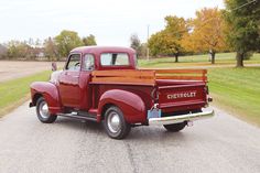 an old red pick up truck parked on the side of a road with trees in the background