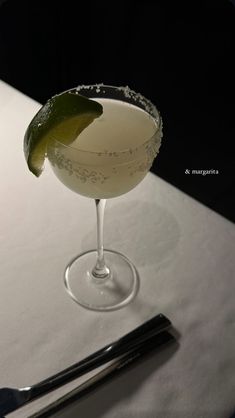 a white table topped with a martini glass filled with liquid and a lime wedge on top of it