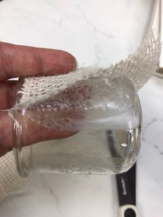 a hand holding a glass jar filled with water on top of a white marble counter