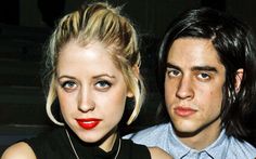 a man and woman sitting next to each other with red lipstick on their lips looking at the camera