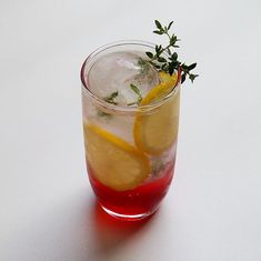 a drink with lemon slices and herbs on the rim, sitting on a white surface