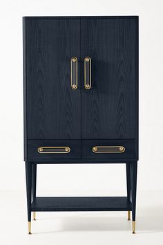 a black cabinet with two brass handles on it's doors and bottom drawer, against a white background