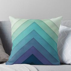 a blue and green throw pillow sitting on top of a gray couch next to pillows