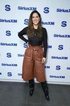 a woman standing in front of a wall wearing brown leather pants and black boots with her hands on her hips