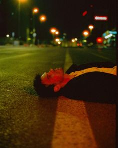 a man laying on the side of a road at night with his head in his hands