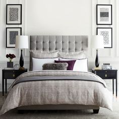 a bedroom with white walls and pictures on the wall above the bed, along with a gray upholstered headboard