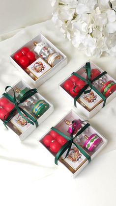 four small boxes with red and green wrapped gifts in them on a white tablecloth