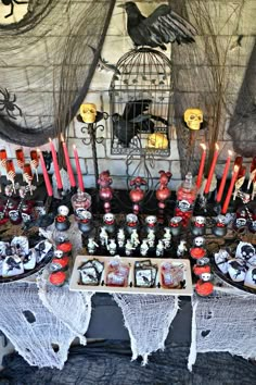 a table topped with lots of halloween treats and candles next to a birdcage