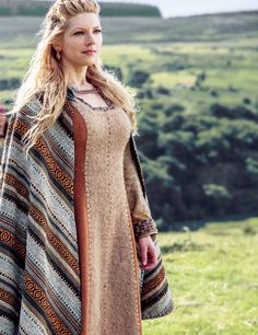 a woman standing on top of a lush green field wearing a long dress and coat