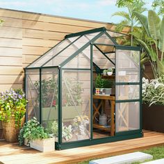 a small green house sitting on top of a wooden deck next to plants and potted plants