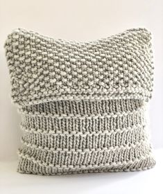 a gray knitted pillow sitting on top of a white table next to a wall