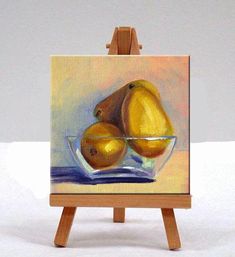 a small easel with a painting of two pears in a glass bowl on it