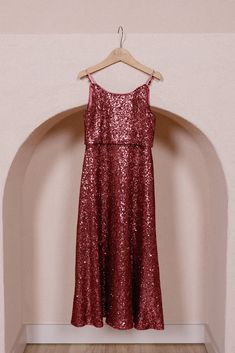 a red dress hanging on a hanger in front of a pink wall and wooden floor